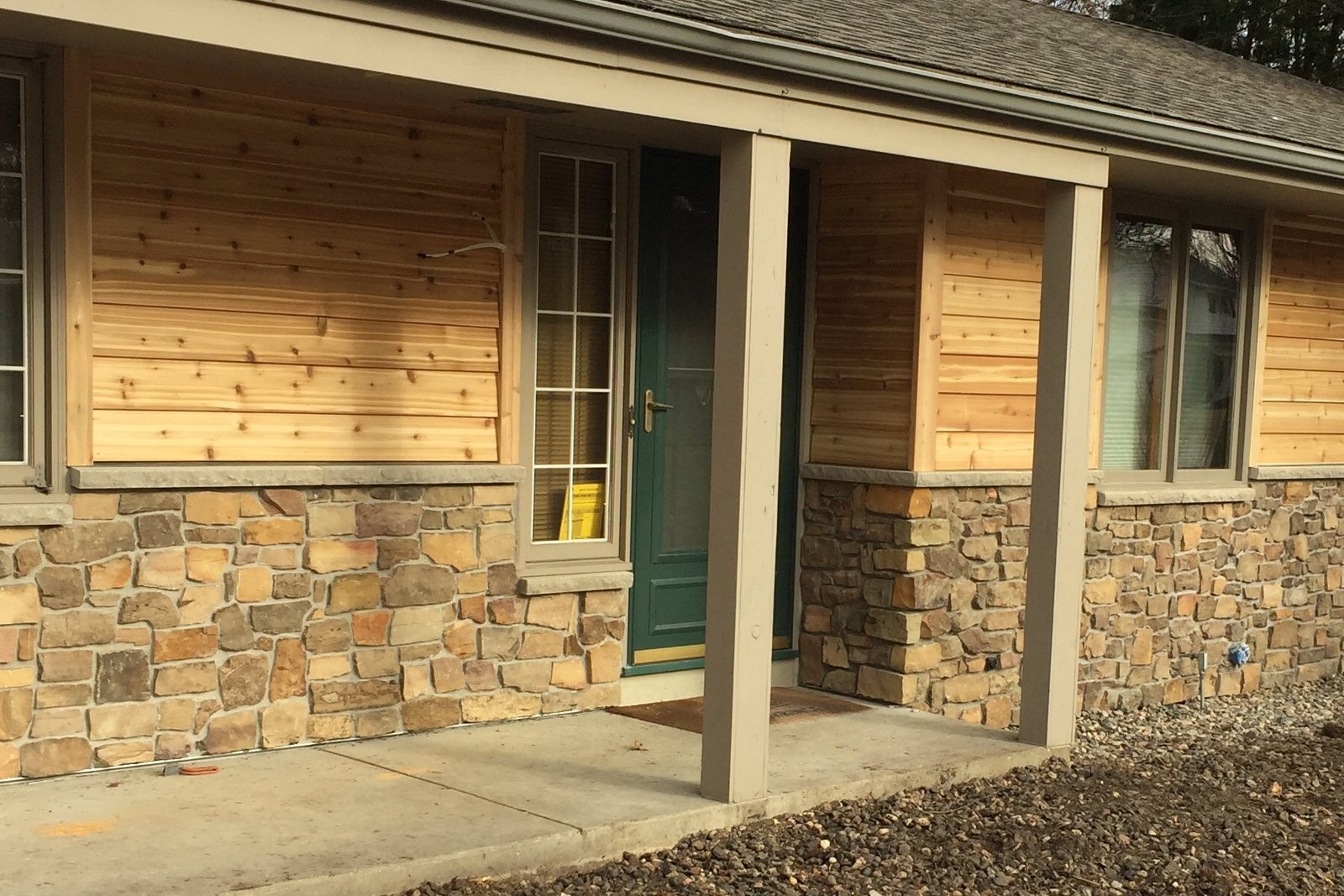 Green entry door with a full-view storm door between new cedar siding and stone