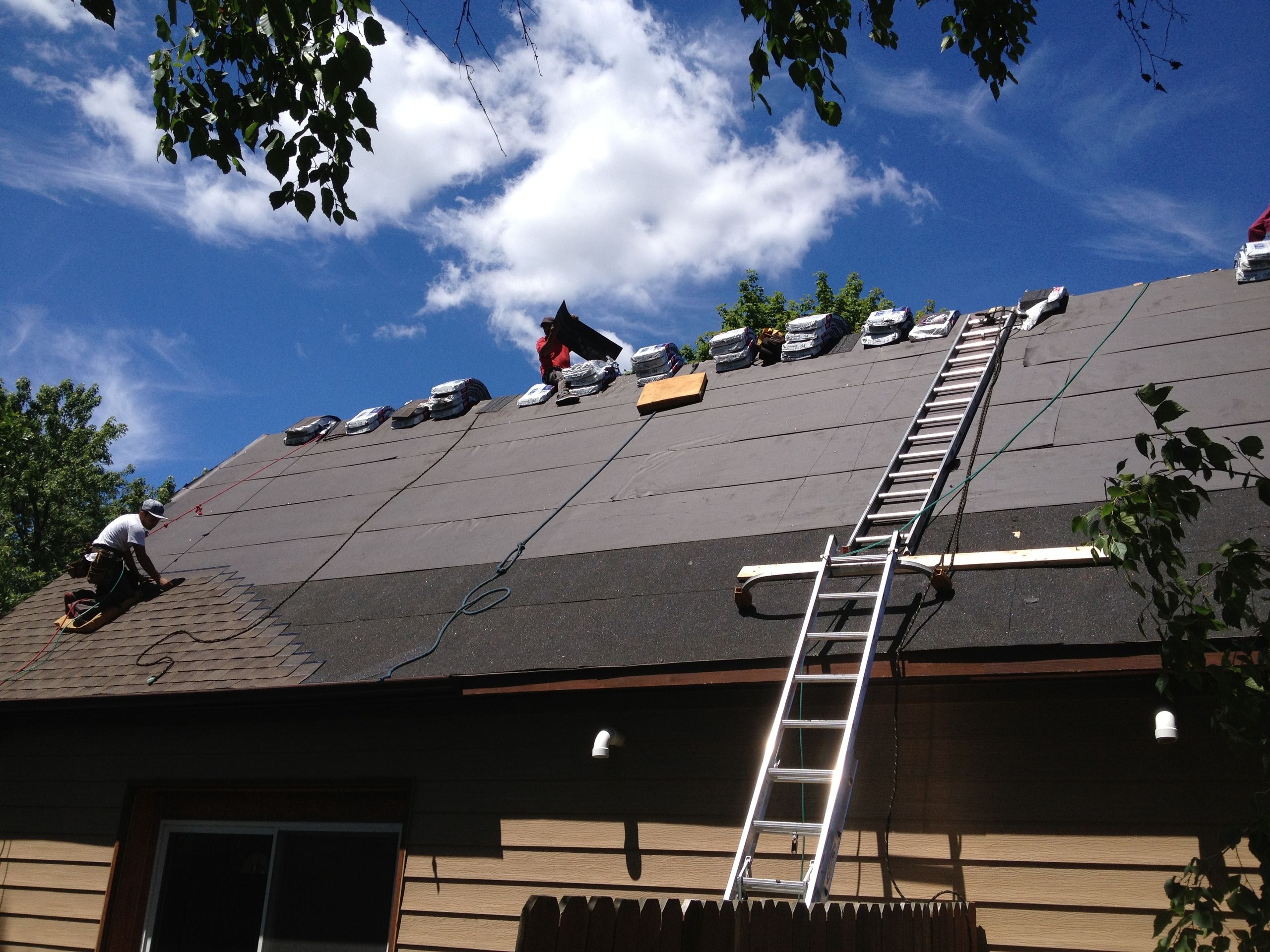 Crew laying underlayment and shingles on a two-story roof