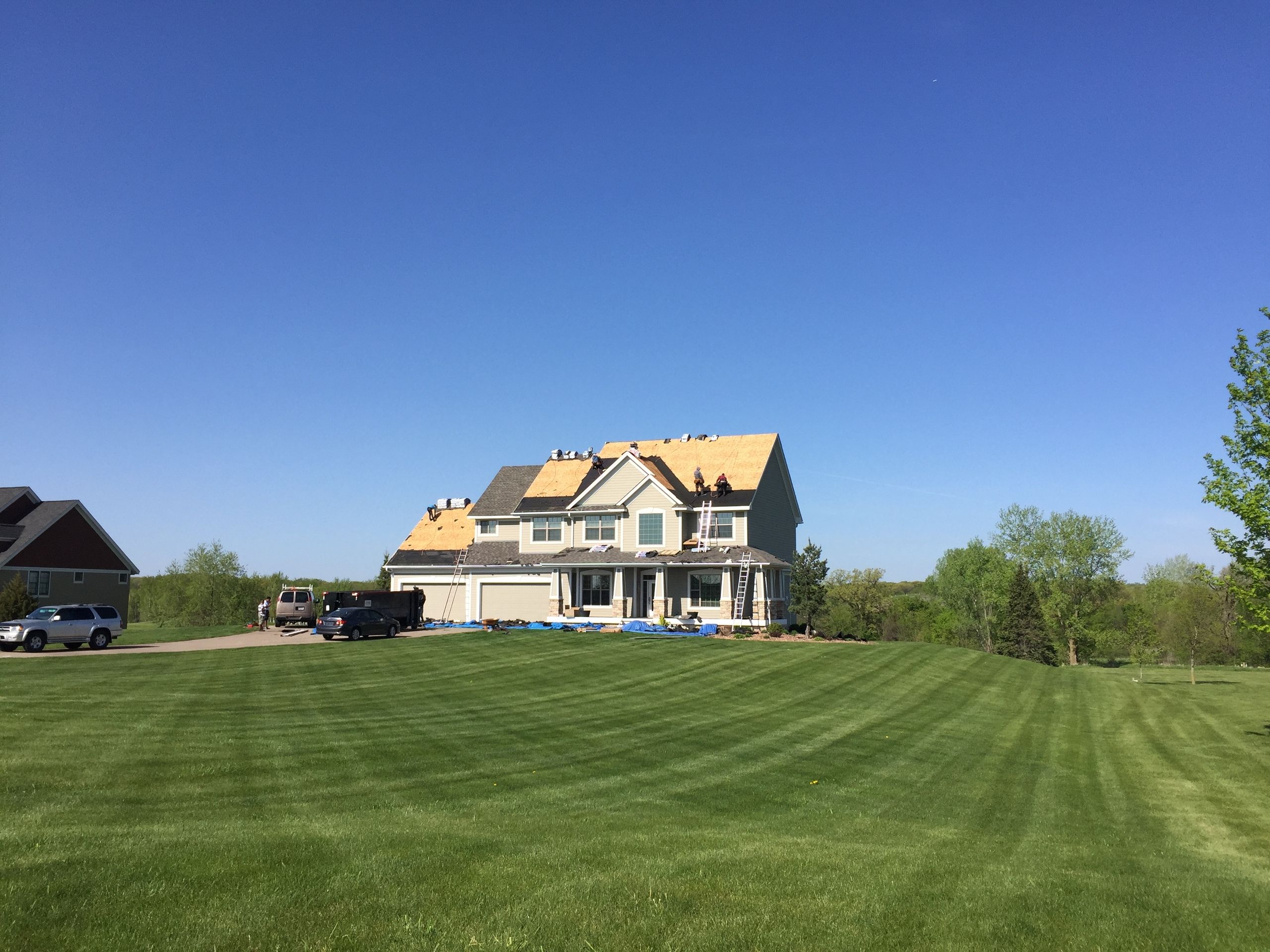 White two-story farmhouse with new roofing across a wide lawn