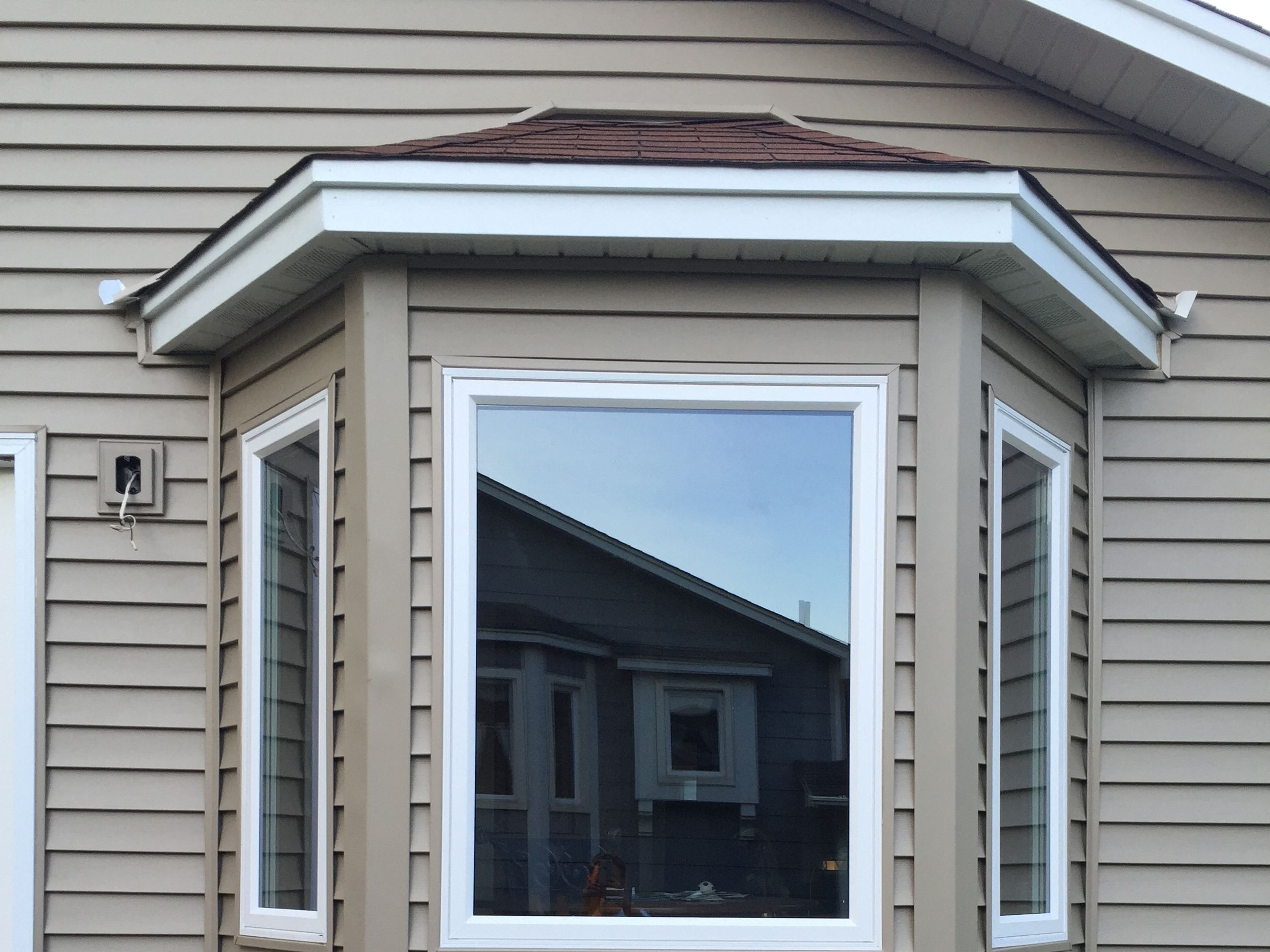 Bay window with three new units under a hip roof on tan lap siding