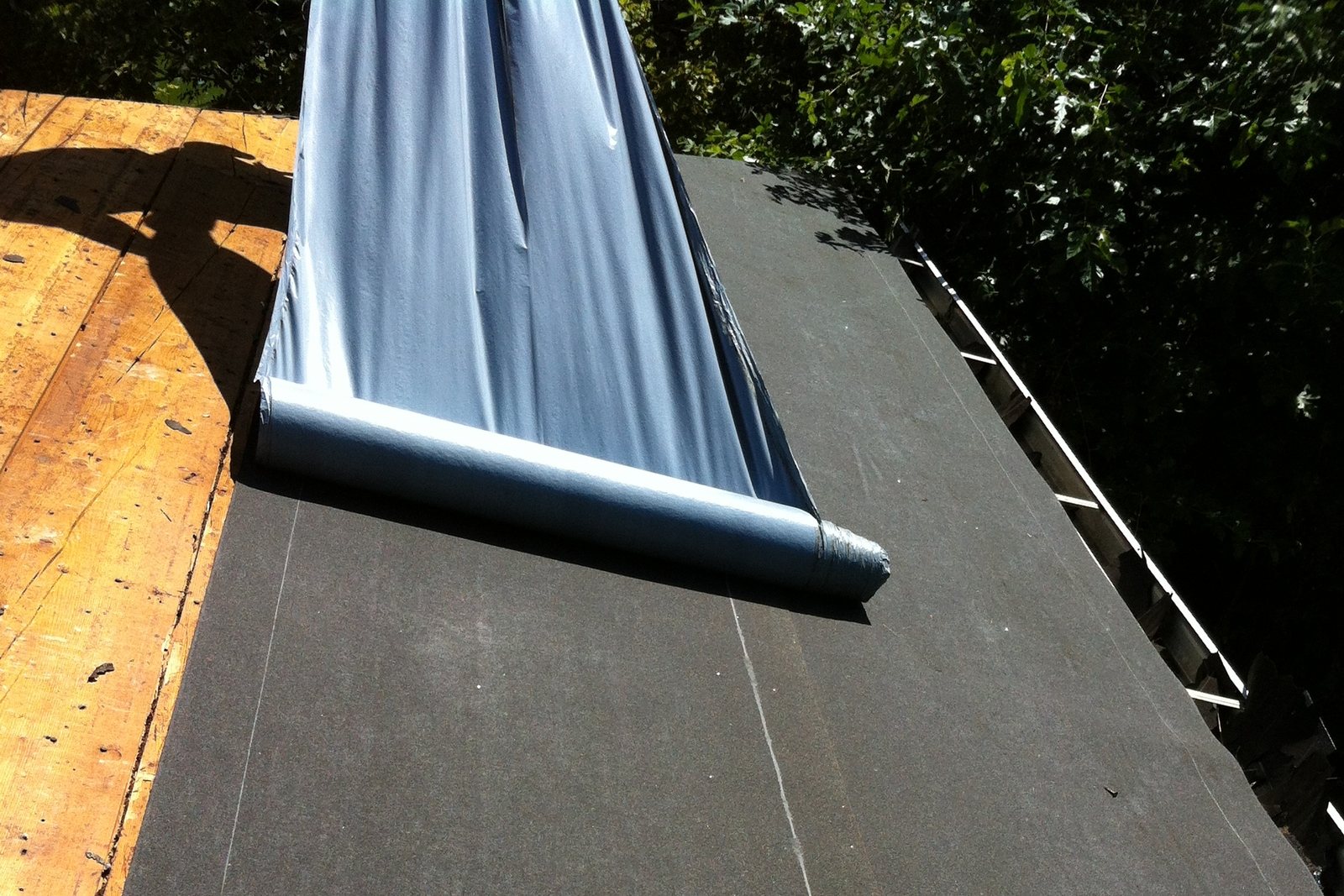 Underlayment rolled out over bare roof decking along the eave