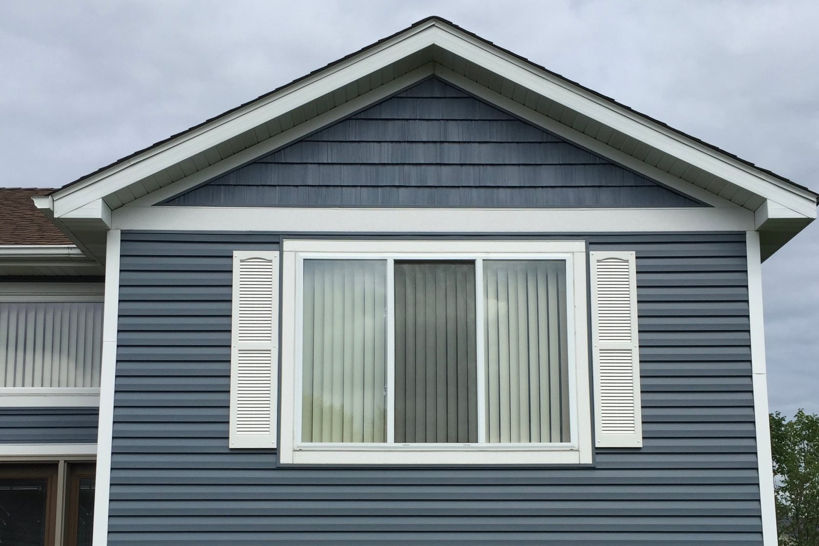 New white-trimmed window in a blue lap siding gable