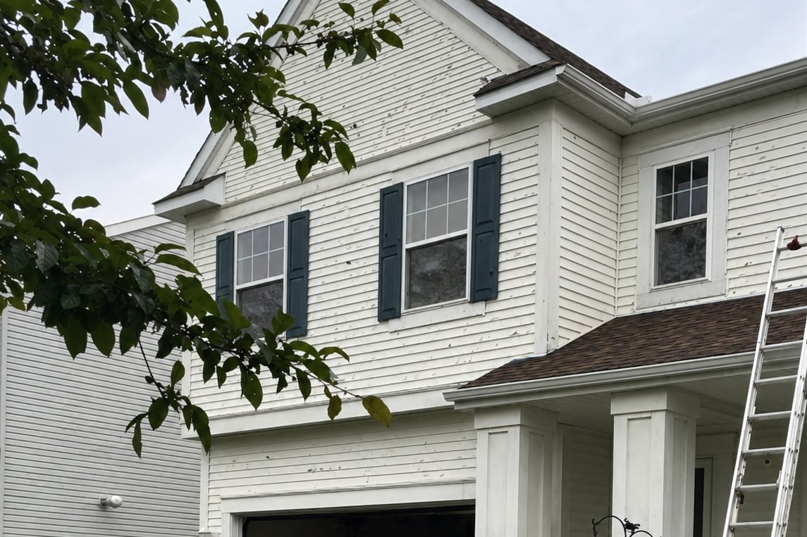 White lap siding pocked with hail impact marks across a two-story wall